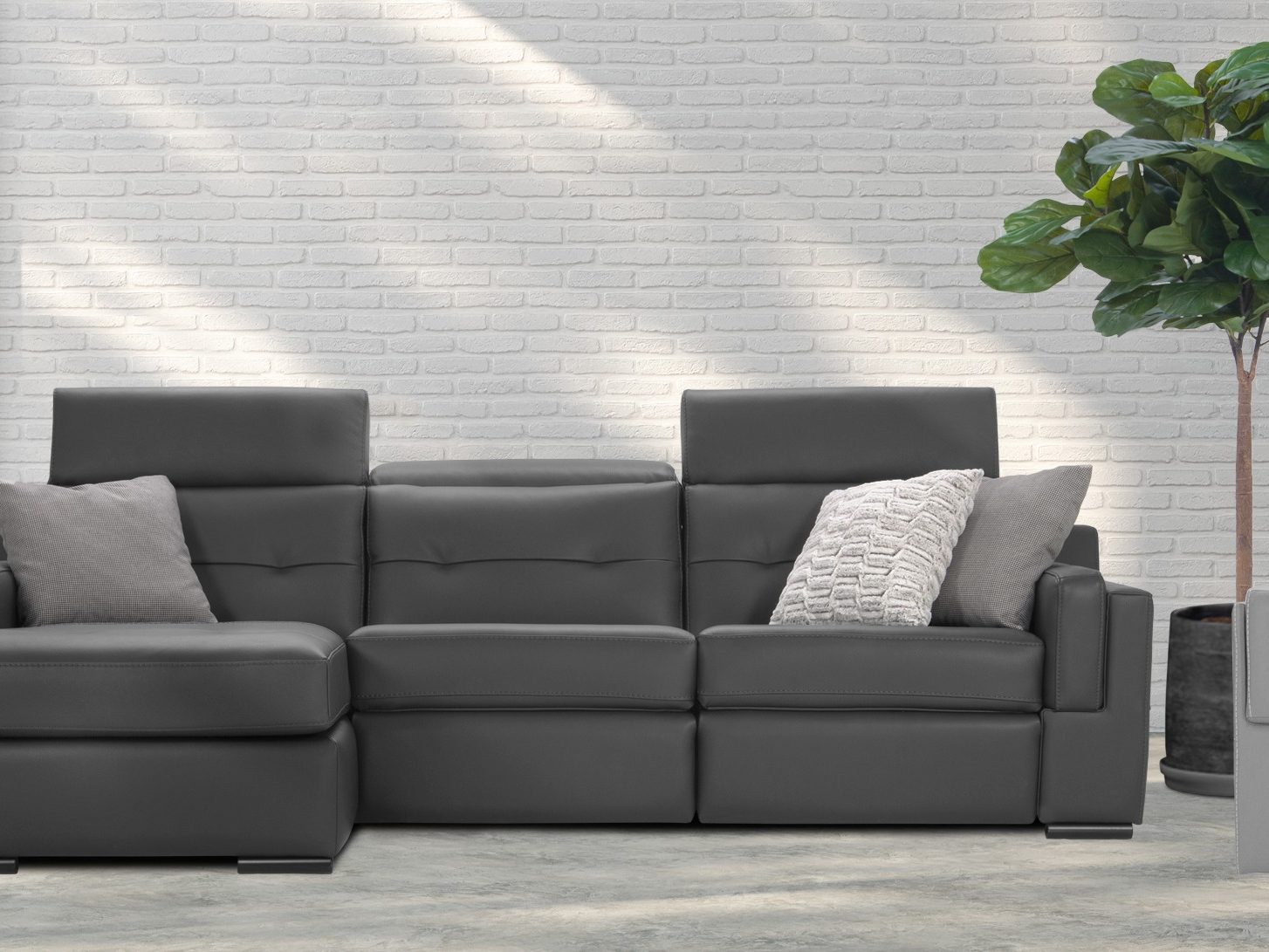 Un sectionnel gris foncé et un fauteuil pivotant gris pâle de la collection Optima devant un mur de brique blanche