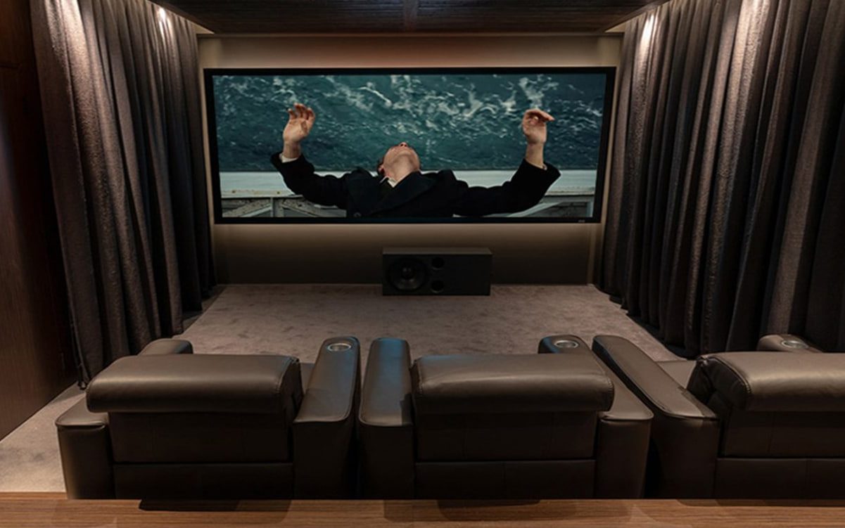 Une salle de cinéma-maison aux rideaux sombres, deux rangées de fauteuils inclinables en cuir brun face à l'écran